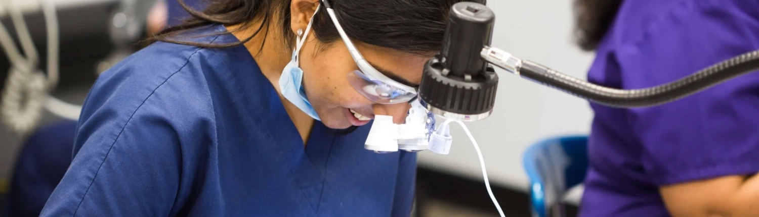 sds-international-bench-prep-hero-desktop-21x9 International dental student preparing a bench exam model under magnification during hands-on training